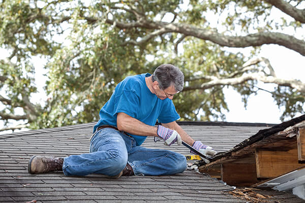 Man using crowbar to remove rotten wood from leaky roof. 
